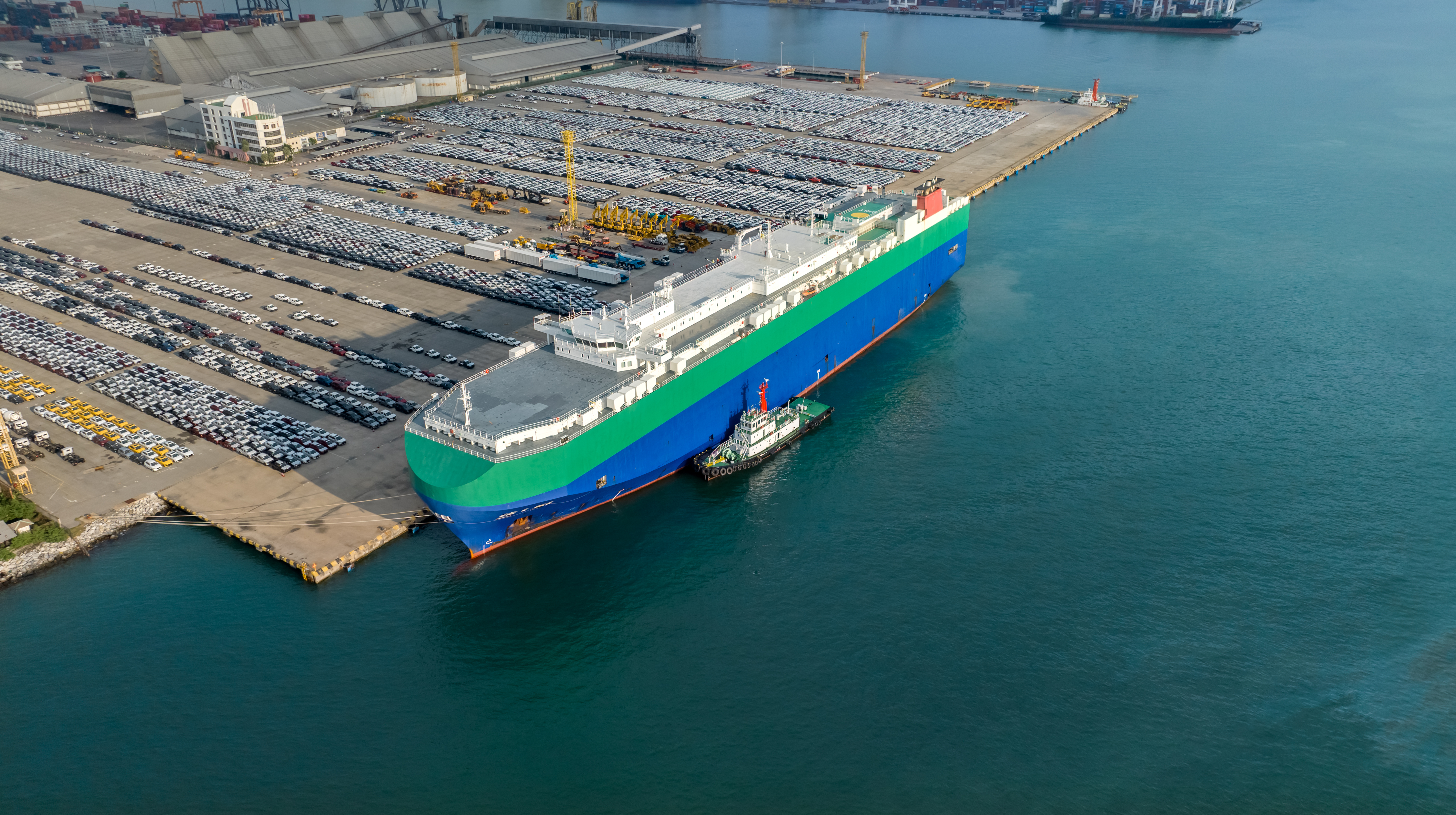 A ship next to a shipping dock filled with JDM cars. 