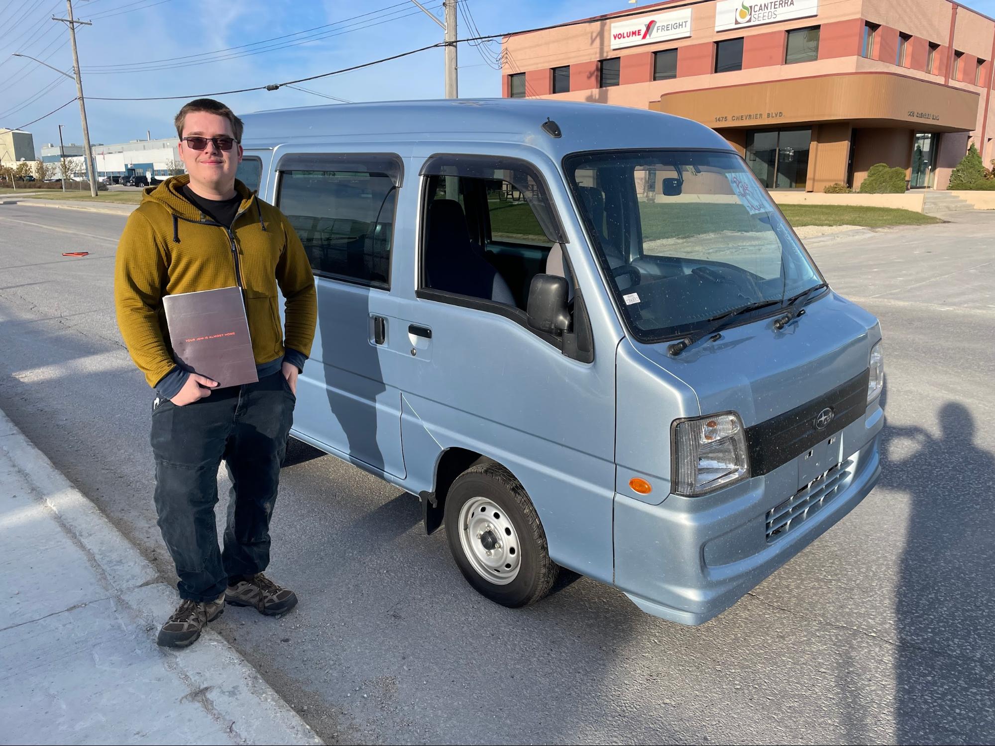 A man standing next to a Subaru Sambar Kei Van. This is one of theJDM vehicles we imported into Canada.