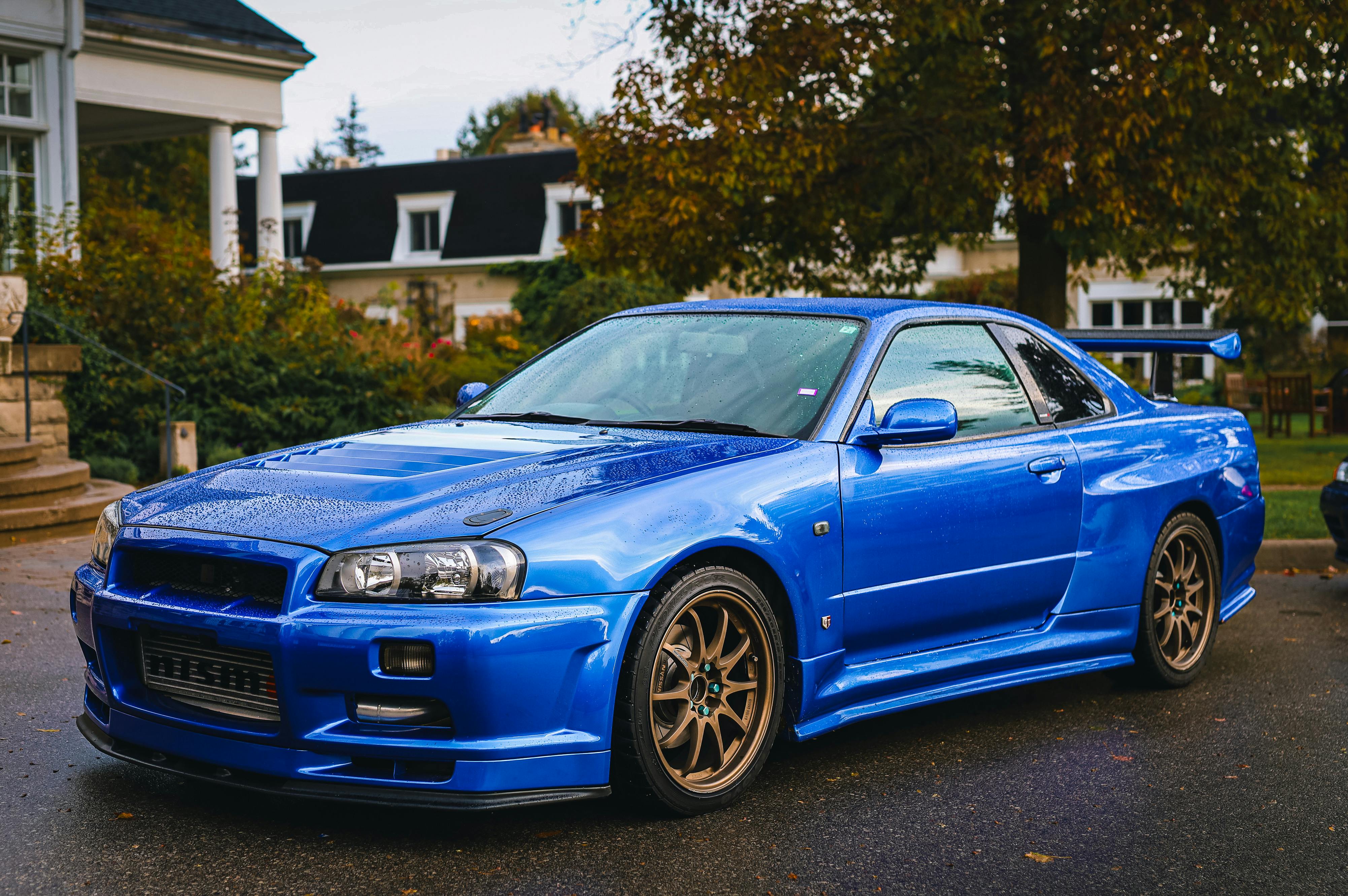 A bright blue Nissan Skyline in front of a house.
