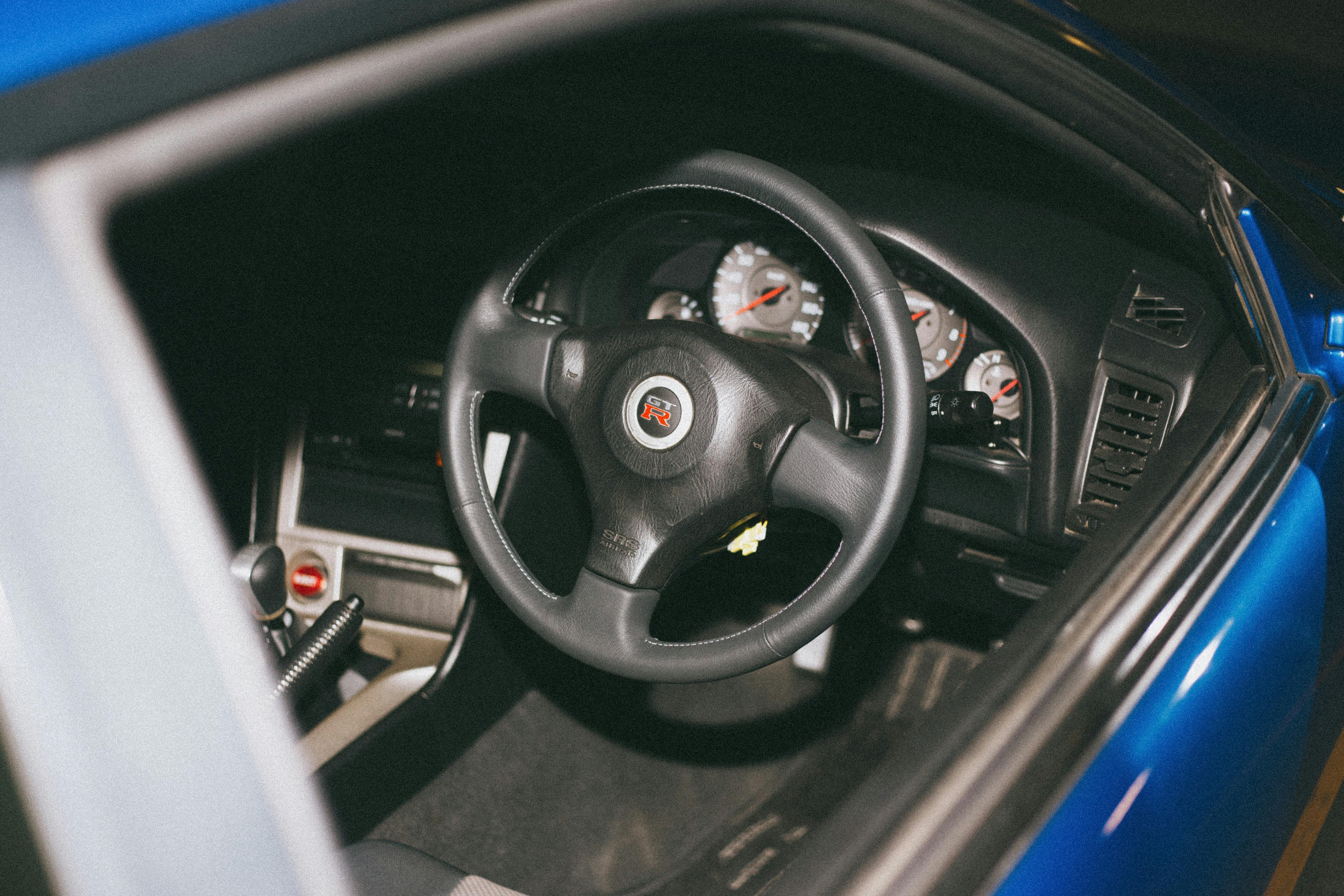 A closeup of a steering wheel through the window of a bright blue Nissan Skyline GTR.