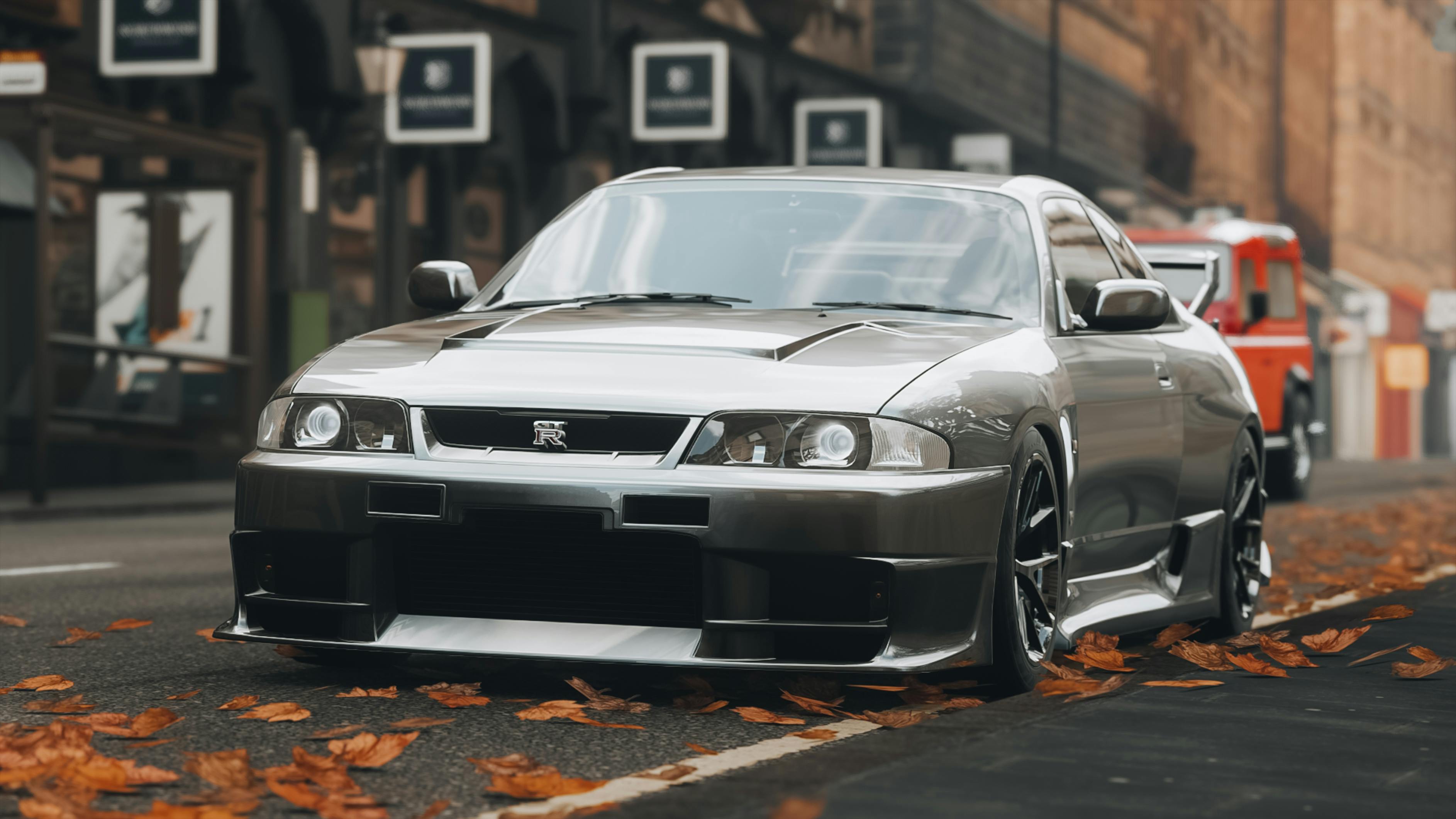A grey Nissan Skyline GTR on a leaf covered city street.