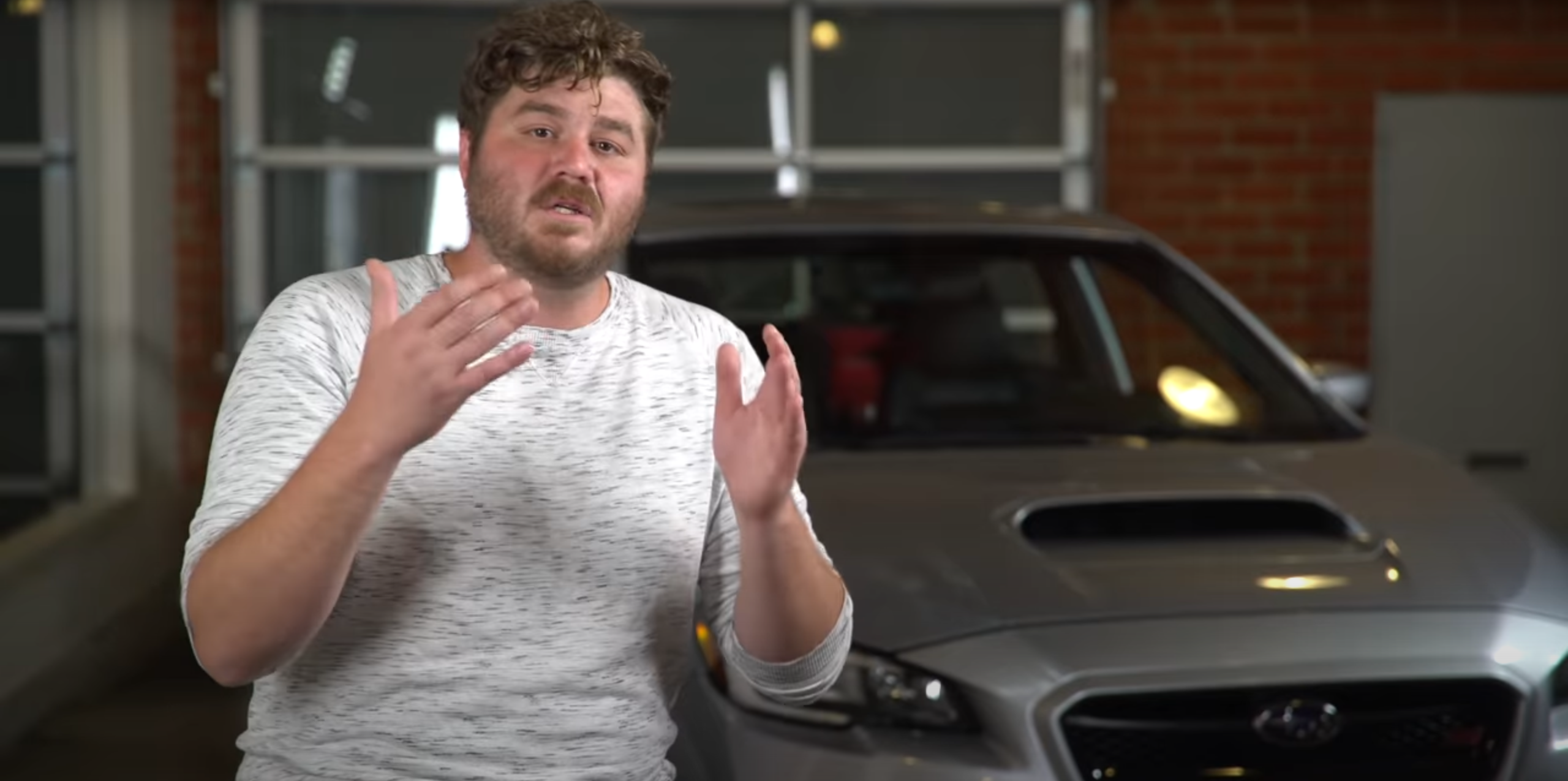 A man with a Subaru WRX STI behind him talking about the car.