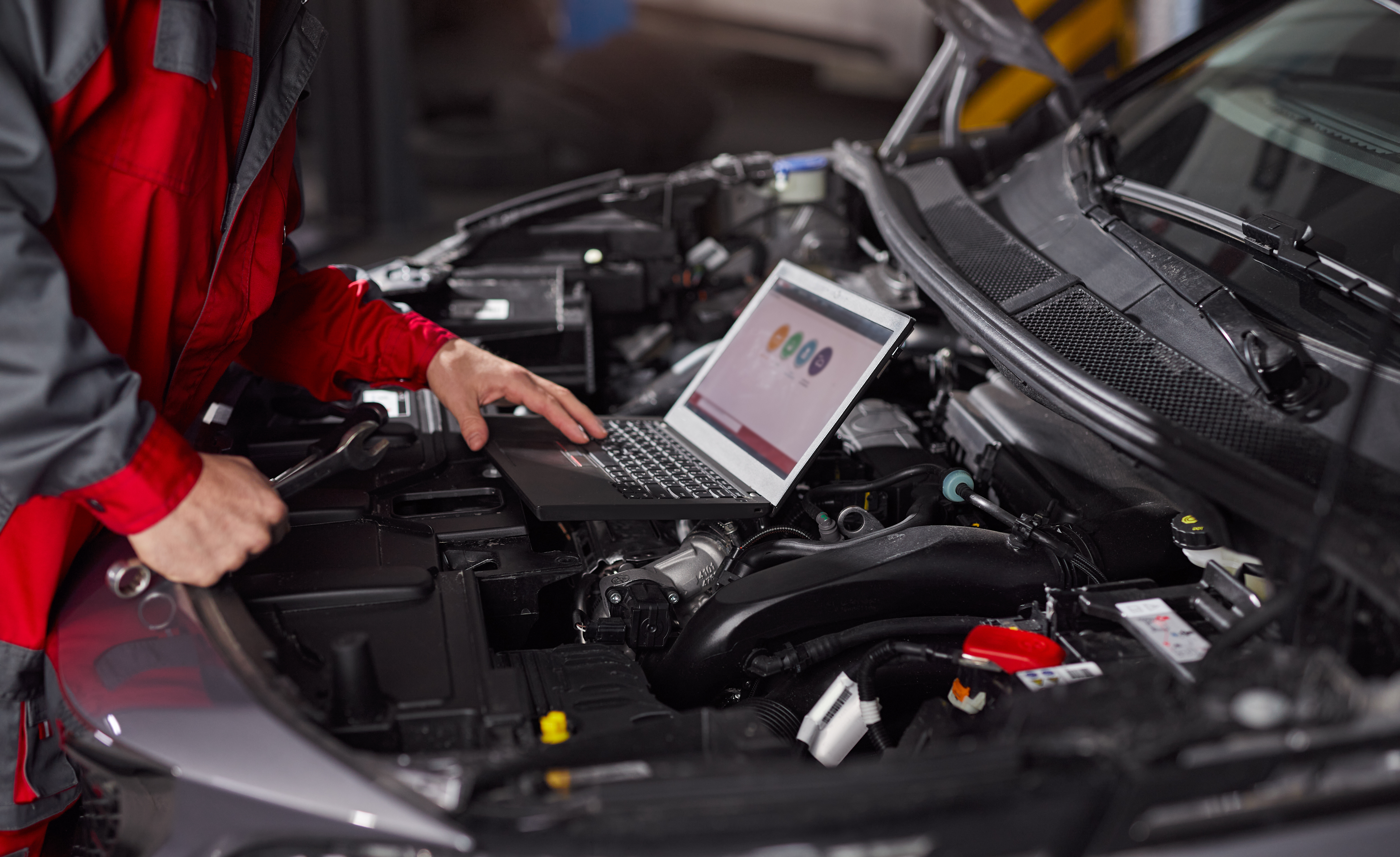 A closeup of a mechanic performing diagnostics on a jdm car, with a laptop open under the hood.