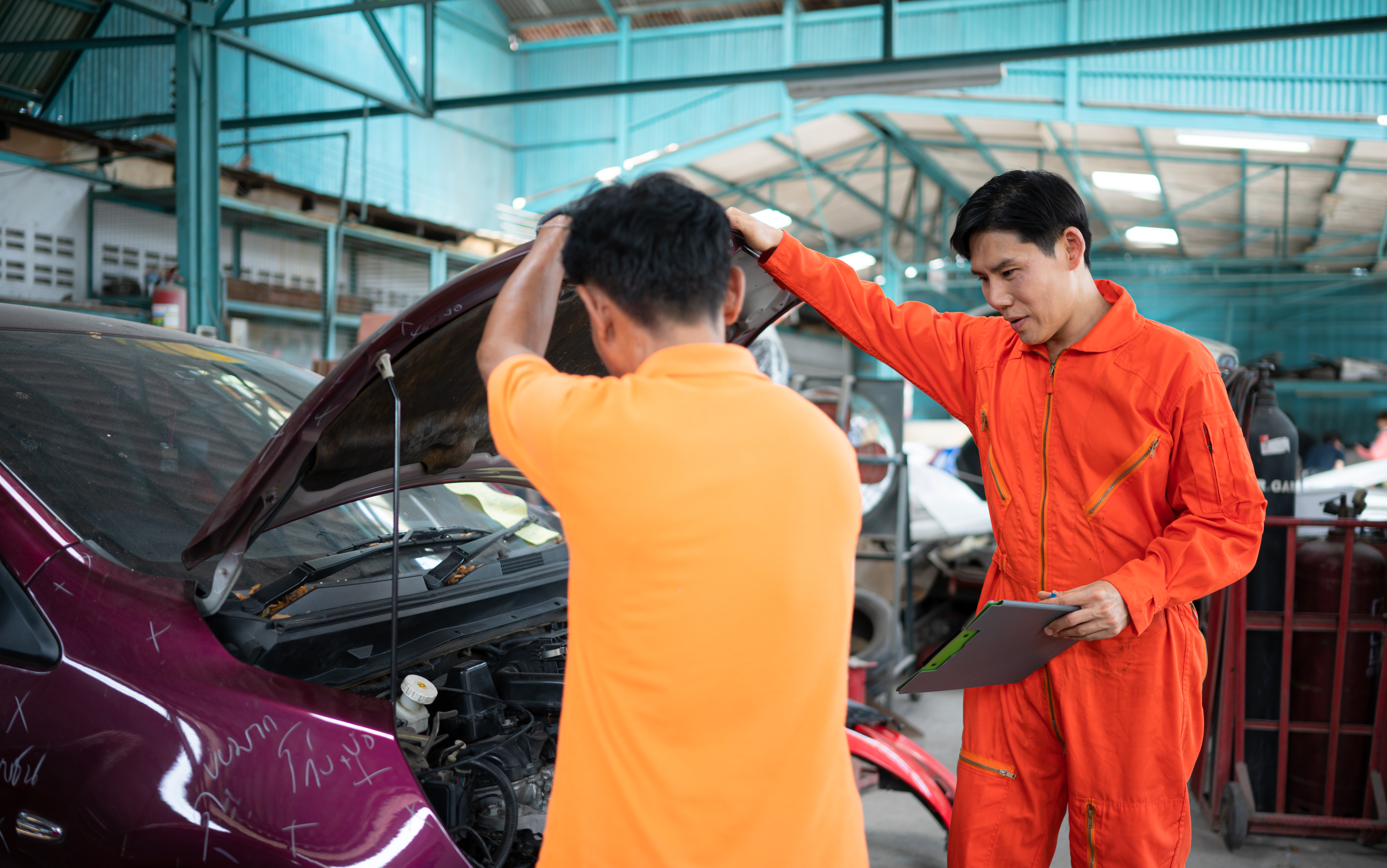 Two mechanics performing a safety inspection on a vehicle, with the hood of the jdm car open.
