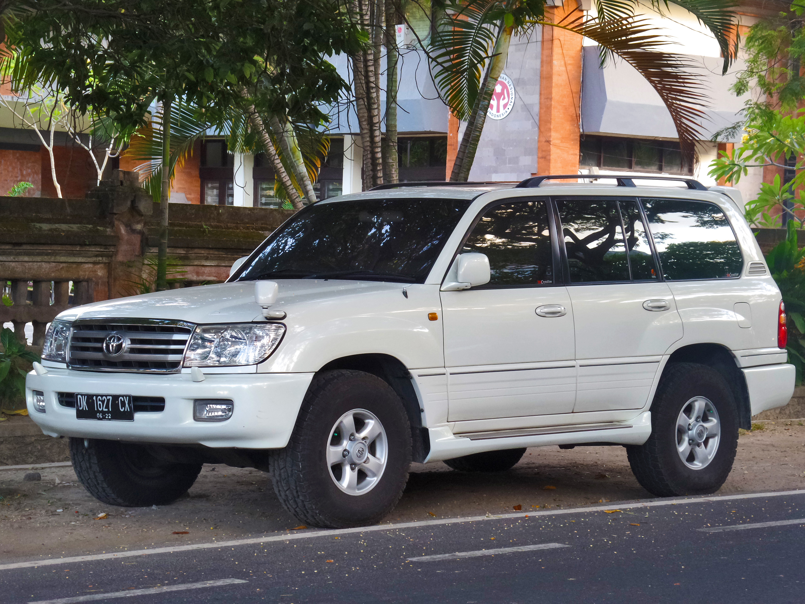  A white Toyota Land Cruiser parked on a street in front of buildings and palm trees. This is a JDM car that can be imported into the USA and Quebec in 2025.