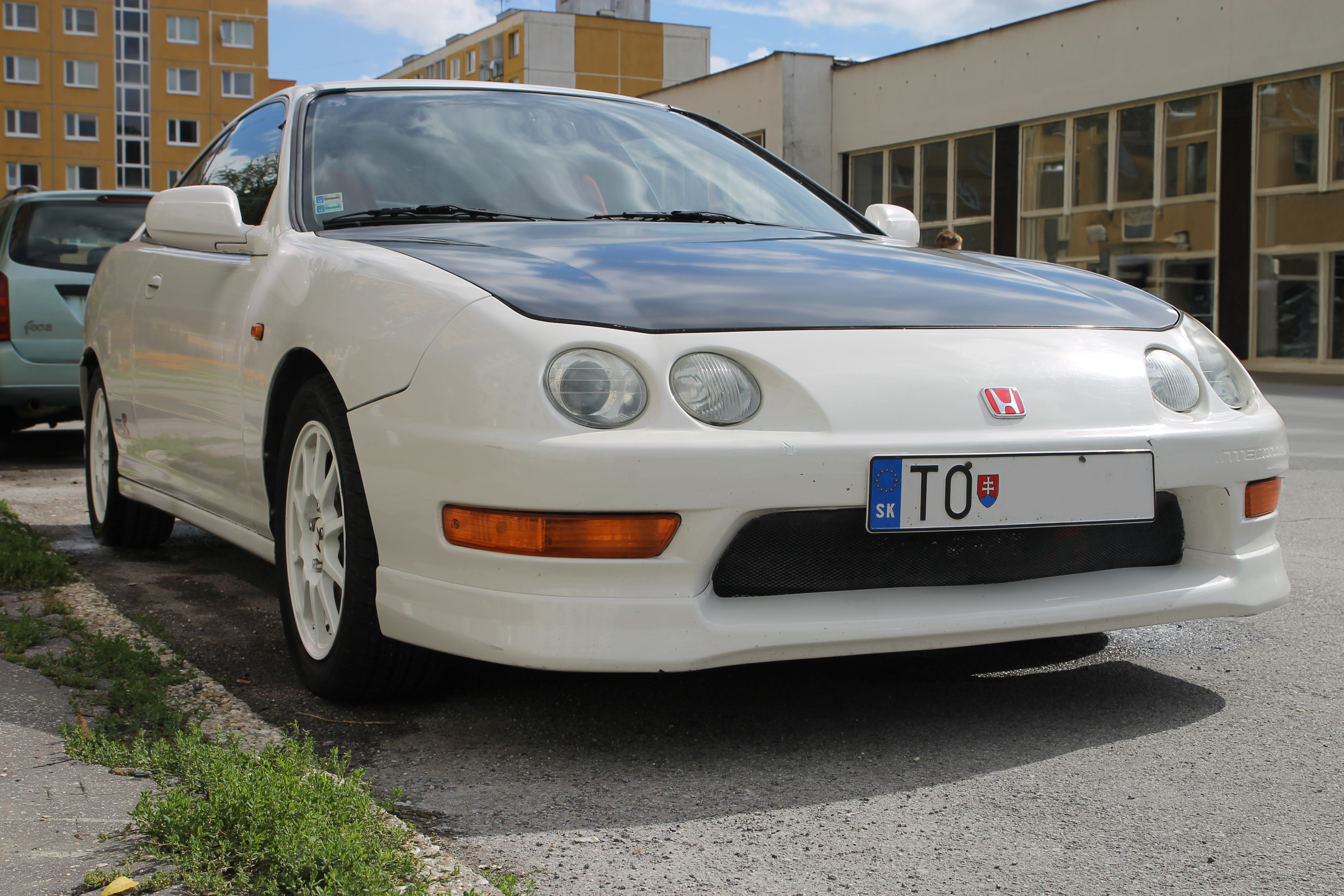A white Honda Integra Type R parked in front of a building. This is a JDM car that can be imported into the USA and Quebec in 2025.