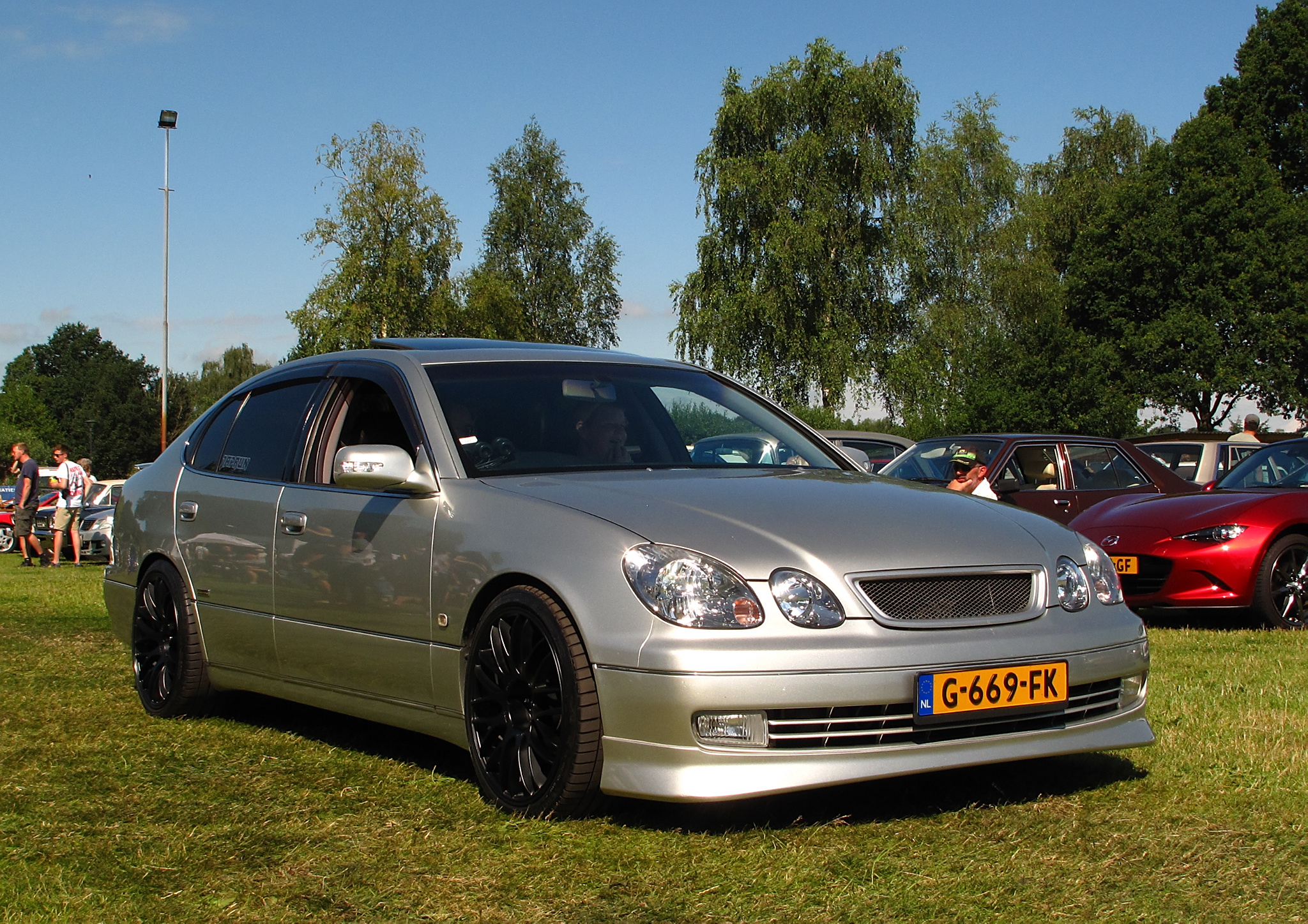 A grey Toyota Aristo V300 parked on a field of grass with other vehicles. This is a JDM car that can be imported into the USA and Quebec in 2025.