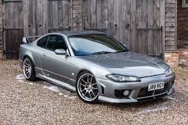 A grey Nissan Silvia S515 Spec R in front of a grey barn door. This is a JDM car that can be imported in the USA and Quebec in 2024.