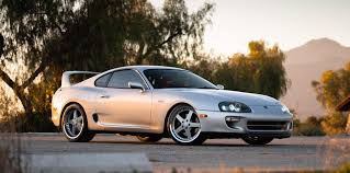 A silver Toyota Supra in front of trees and hills at dusk. This is a JDM car that can be imported in the USA and Quebec in 2024.