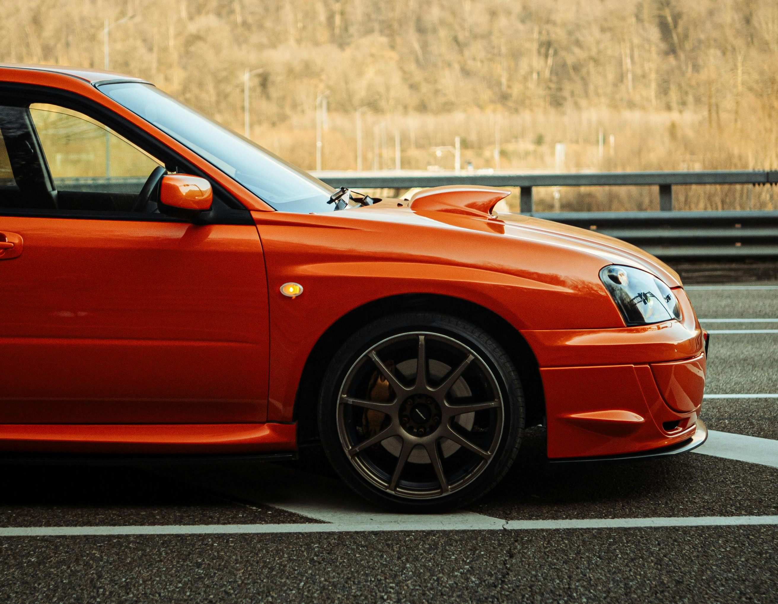 An orange jdm car parked on a highway in Canada with trees in the background.