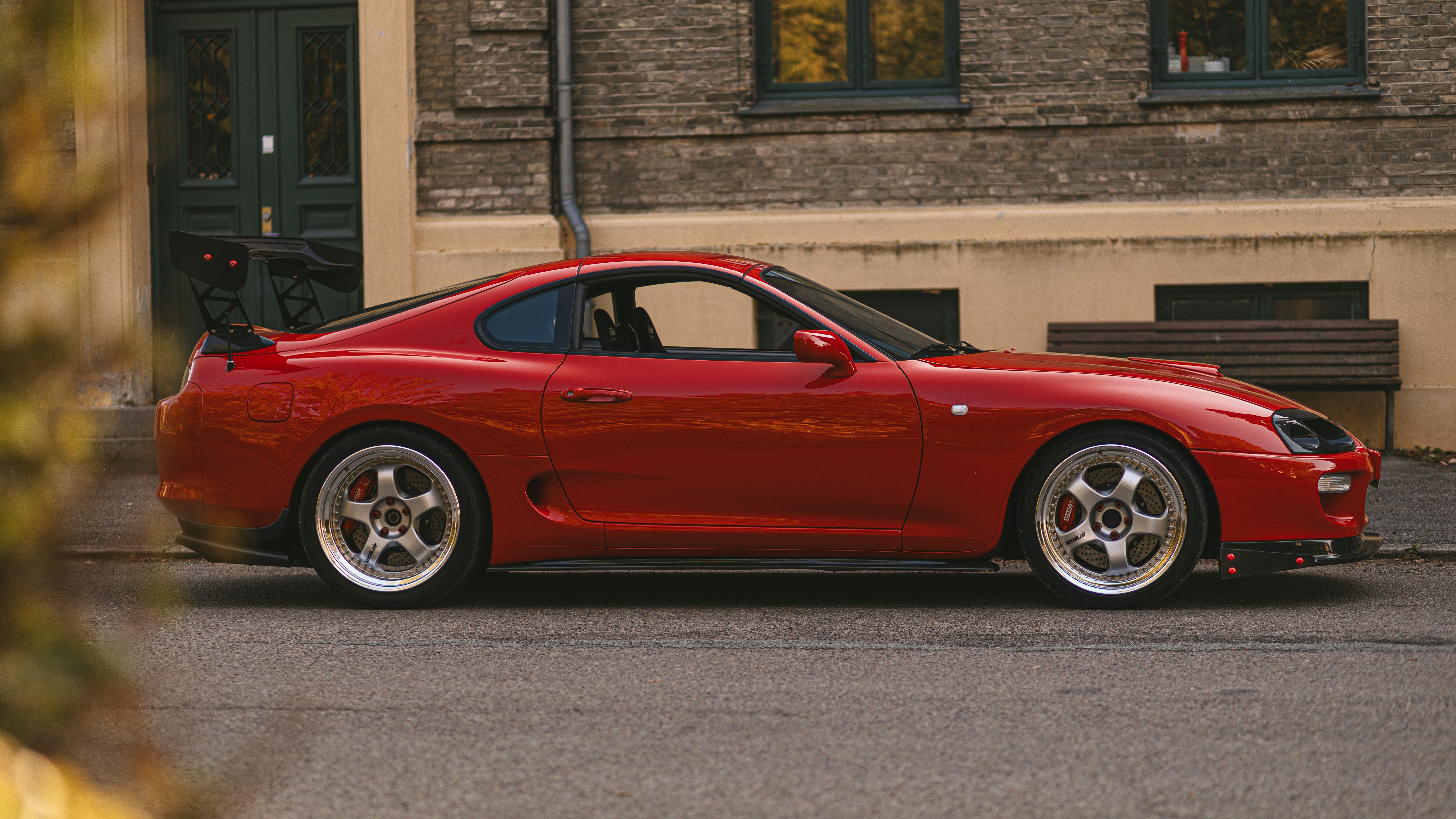 A red JDM sports car parked in front of an apartment building.